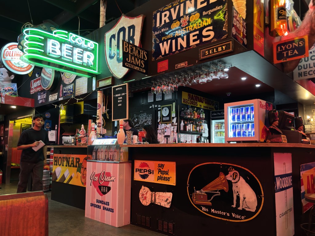 Interior of Fat Bob's Bar Moorabbin. Dark bar crowded with signs and neon green beer sign.