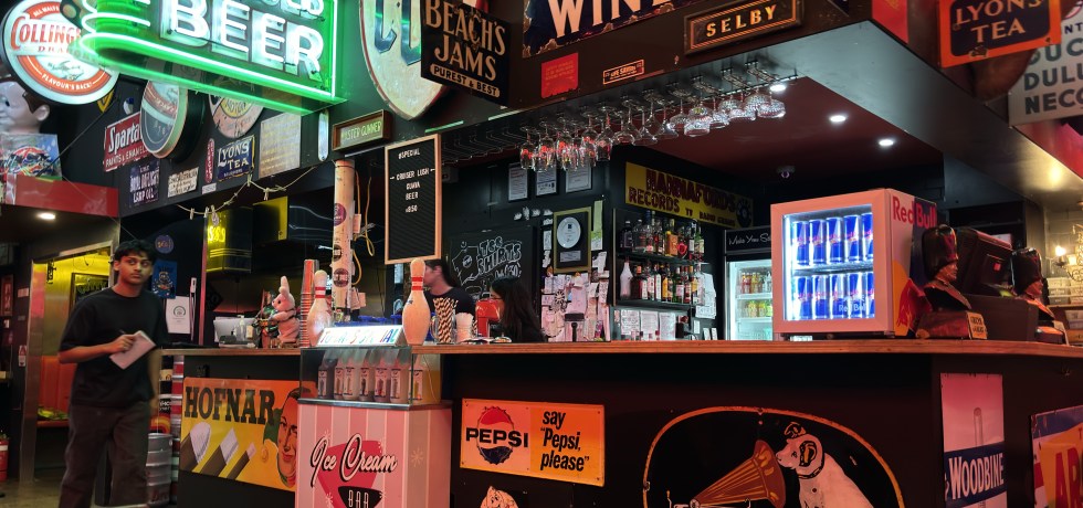 Interior of Fat Bob's Bar Moorabbin. Dark bar crowded with signs and neon green beer sign.