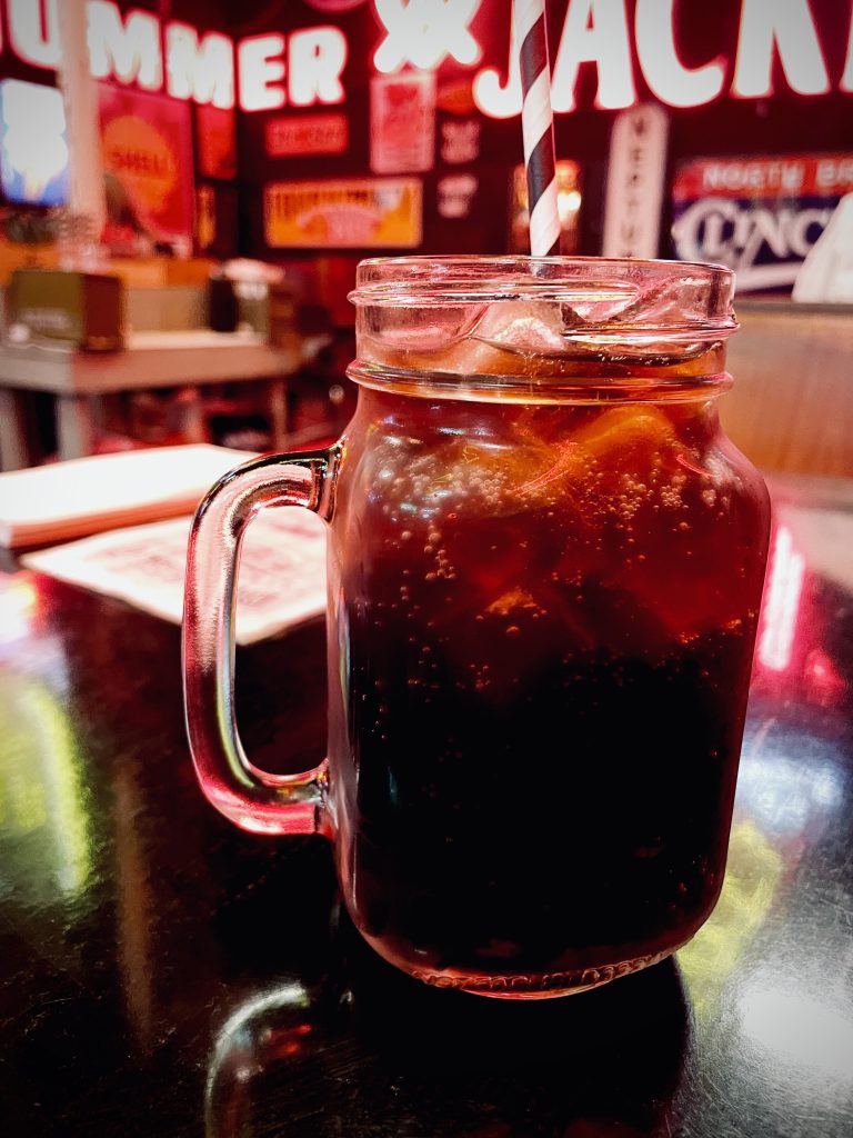 Small pitcher of coke on a dark brown table with neon signs in background at Fat Bob's Moorabbin