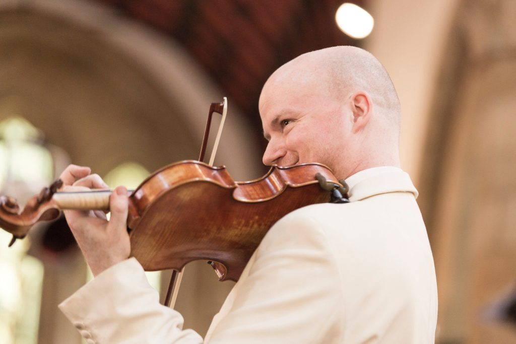 Patrick Savage playing violin in a light coloured jacket