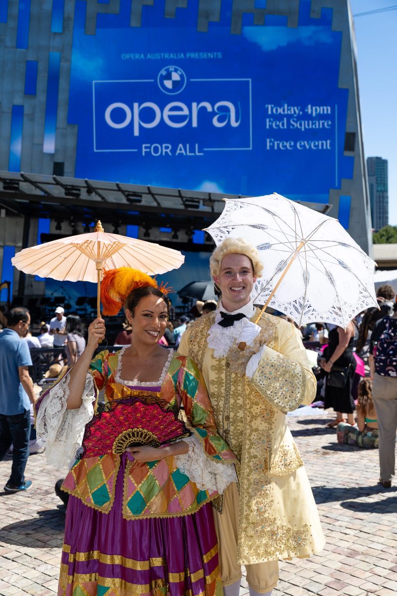Two people with parasols standing in front of blue opera for all sign at BMW opera for all.