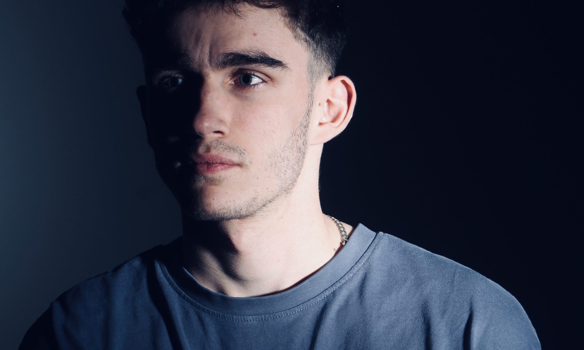 Image of musician Joseph Simon with face half in shadow wearing a blue t-shirt