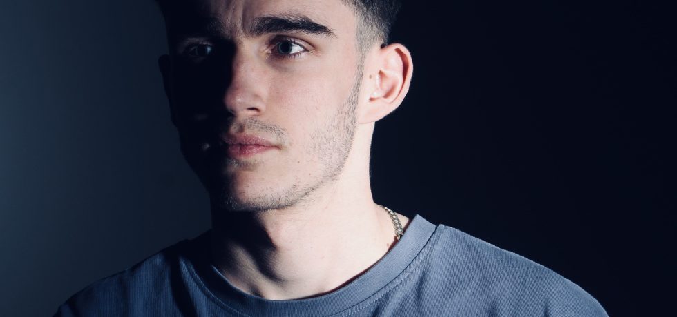 Image of musician Joseph Simon with face half in shadow wearing a blue t-shirt
