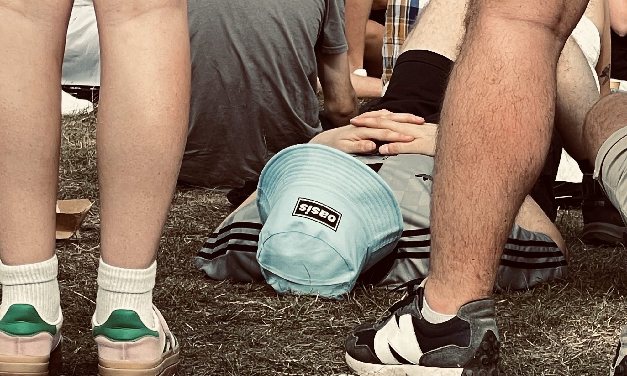 person with Oasis blue bucket hat on lay on the ground at Oasis concert