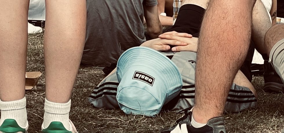 person with Oasis blue bucket hat on lay on the ground at Oasis concert