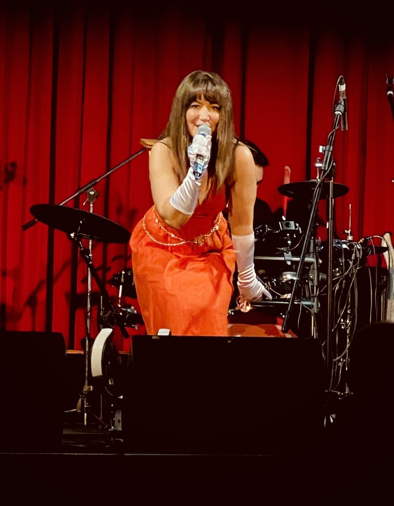 Image of Kat Greta singing against a red curtain at St. Kilda's Memo Music Hall