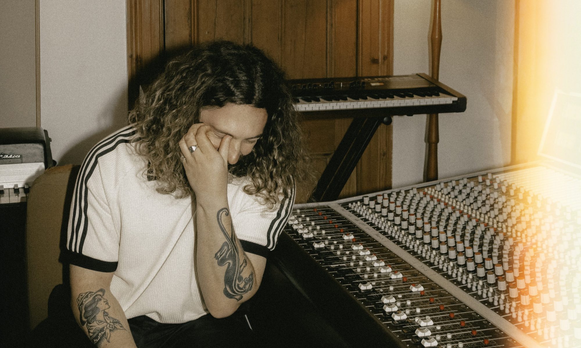 Naarm/Melbourne singer Zachary Leo sat by a mixing desk with his hand covering his face.