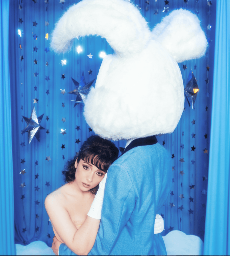 Aleksiah huggins someone with a large white bunny head, in front of a blue backdrop. Promo image for single Faker.