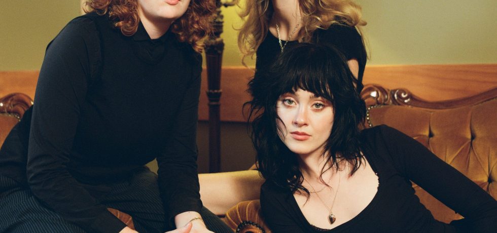 Band Folk Bitch Trio dressed in black sat on sofas