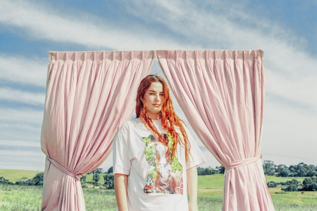 Singer Mia Wray in front of a pink curtain taken in a field