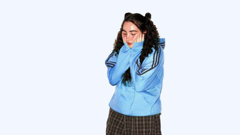 Charli Lucas with her hands to her face wearing a blue adidas jacket. EP cover for i shouldnt but i love you