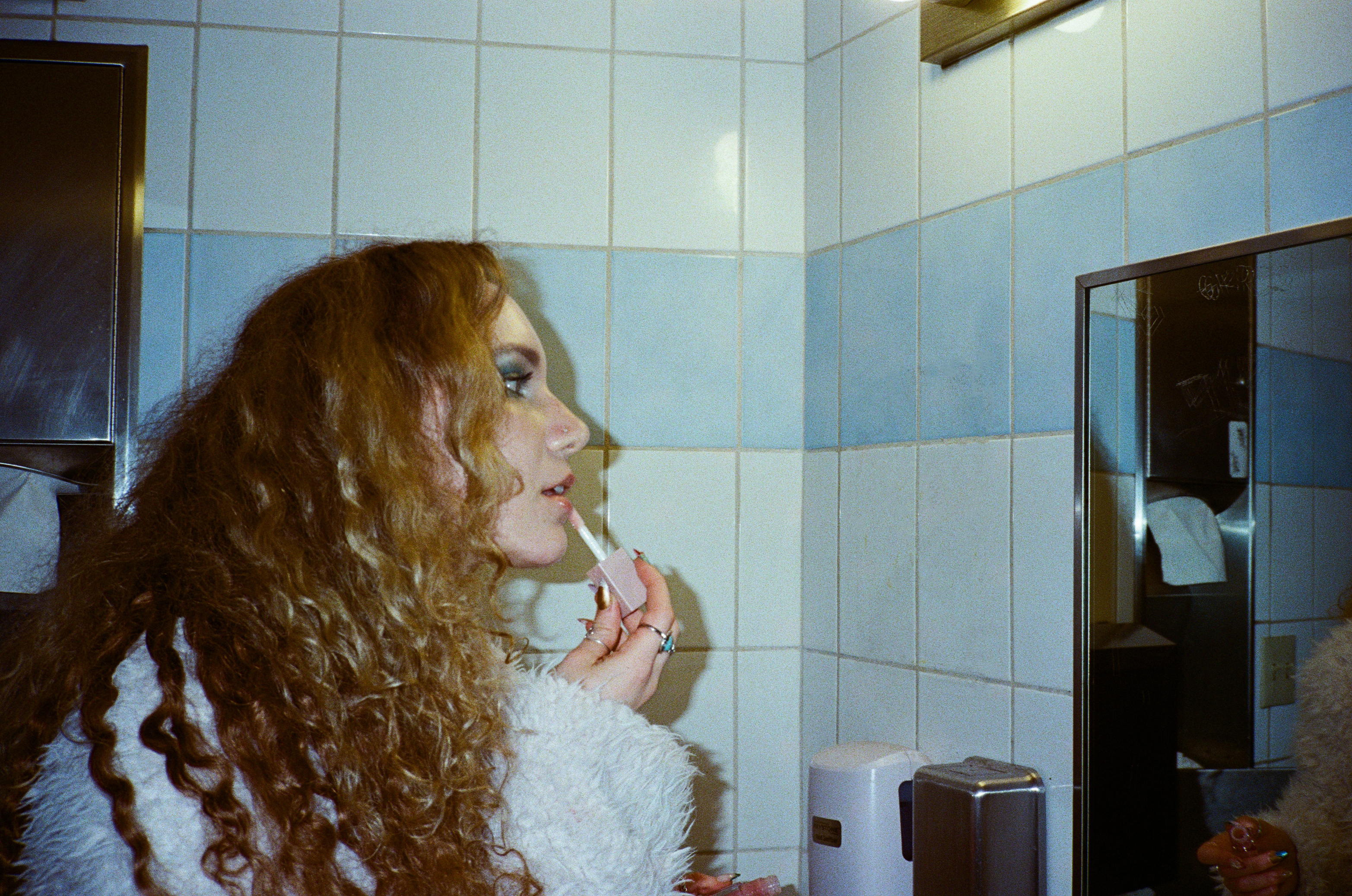 Image of Emily James applying make up in a bathroom. 