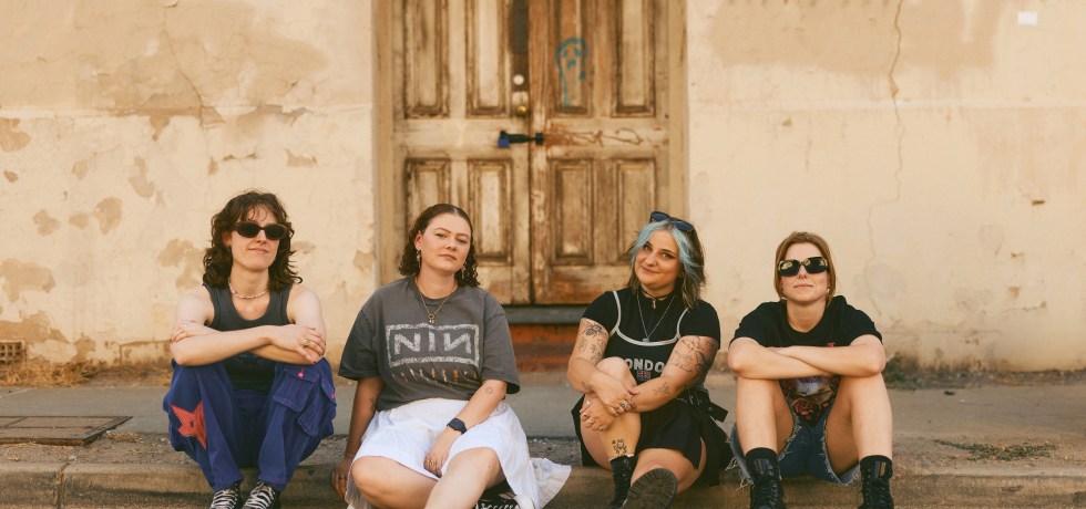 Image of Adelaide Band Oscar The Wild, sat on the floor in front of a light wall and a wooden door