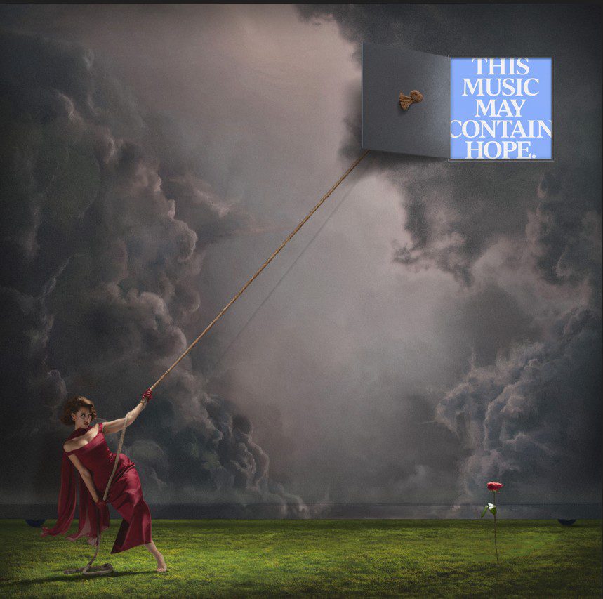 Image of a woman against a dark stormy sky opening a door in the sky to reveal thr words This Music May Contain Hope. RAYE album cover