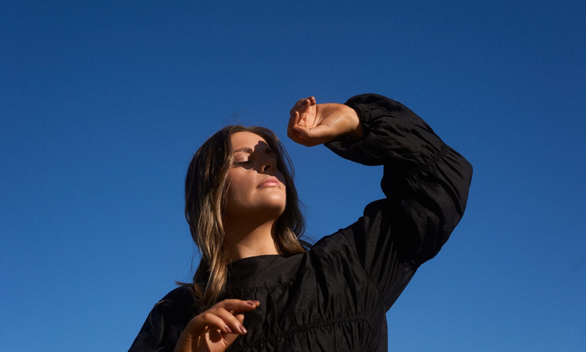 Image of Melbourne singer Sidney with her hand sheilding her face taken against a bright blue sky. EP cover for what if it ends.