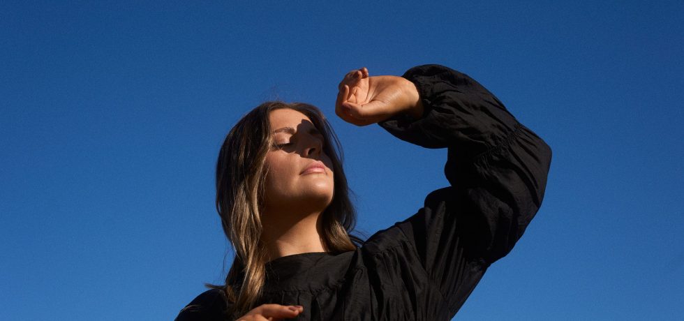 Image of Melbourne singer Sidney with her hand sheilding her face taken against a bright blue sky. EP cover for what if it ends.