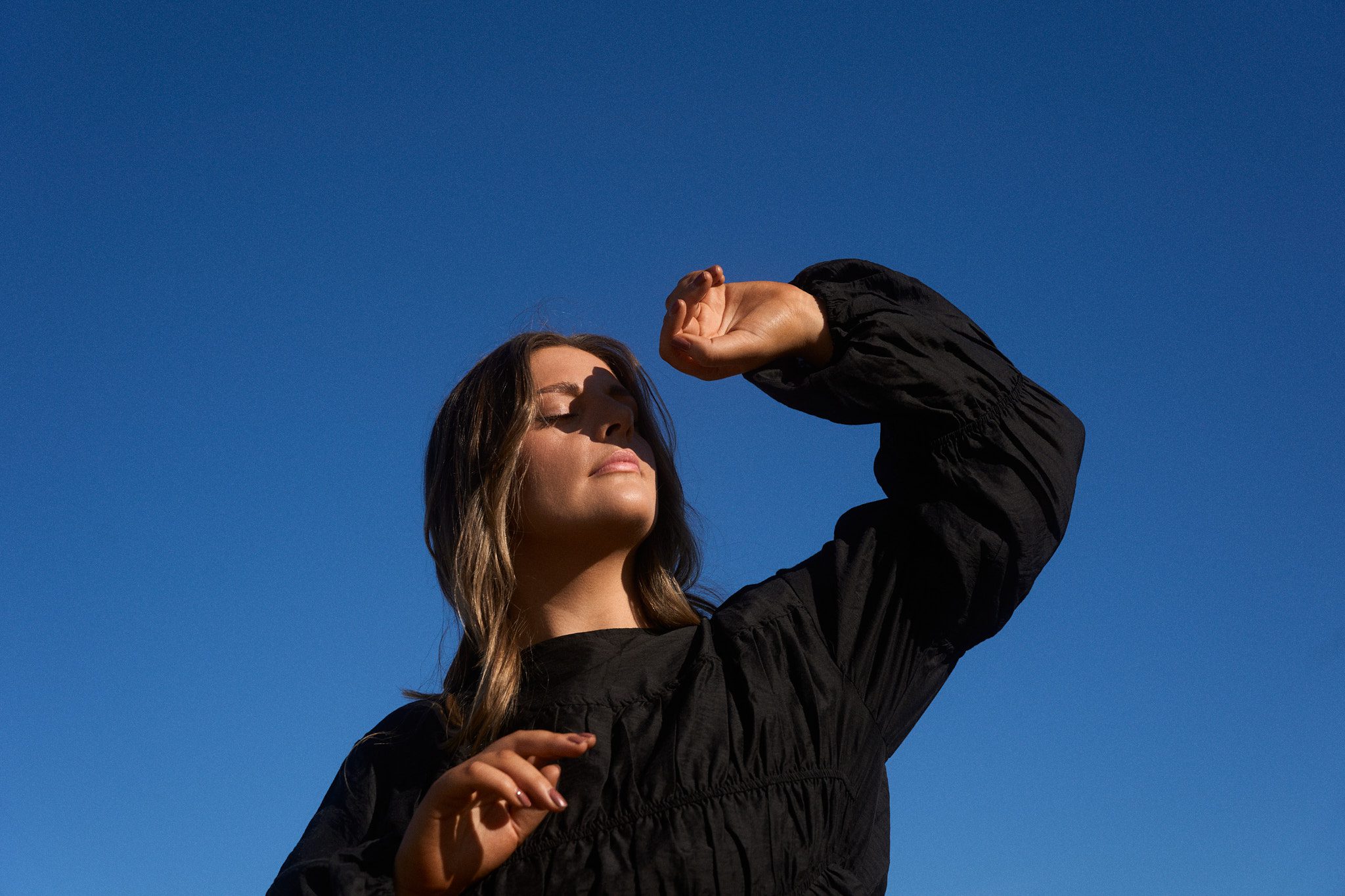 Image of Melbourne singer Sidney with her hand sheilding her face taken against a bright blue sky. EP cover for what if it ends.