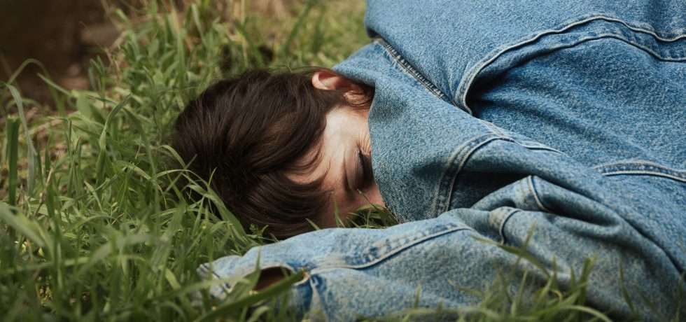 Image of singer Anna Jeavons laying in the grass with an oversized blue top covering half of her face. Single cover for Smart Casual