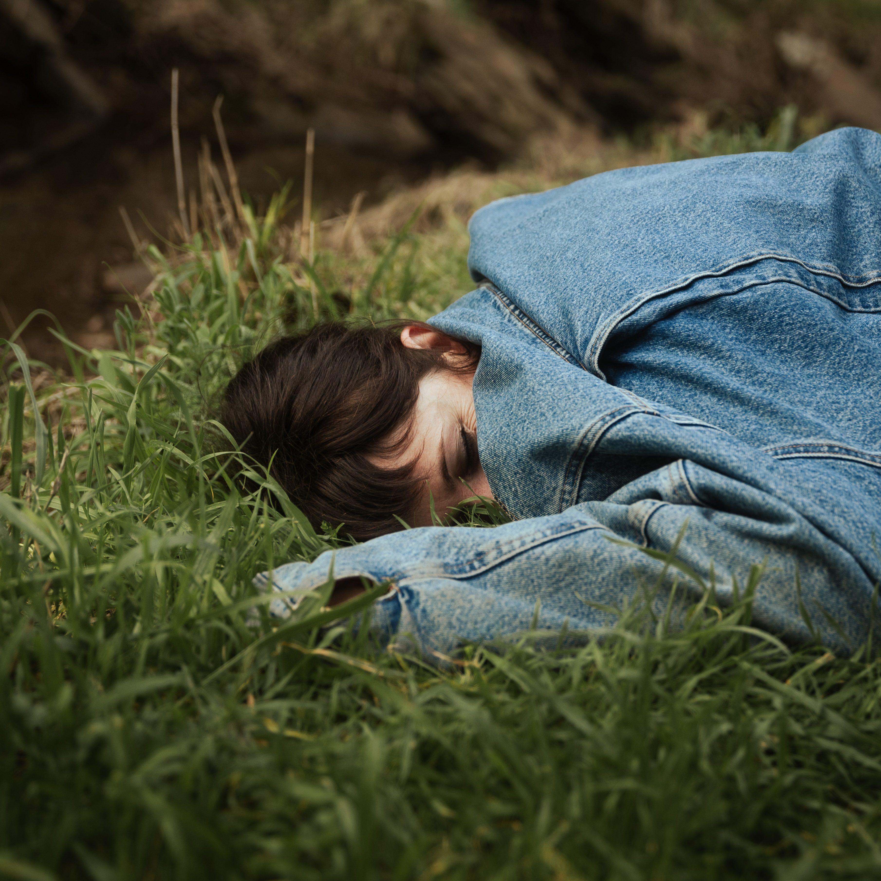 Image of singer Anna Jeavons laying in the grass with an oversized blue top covering half of her face. Single cover for Smart Casual