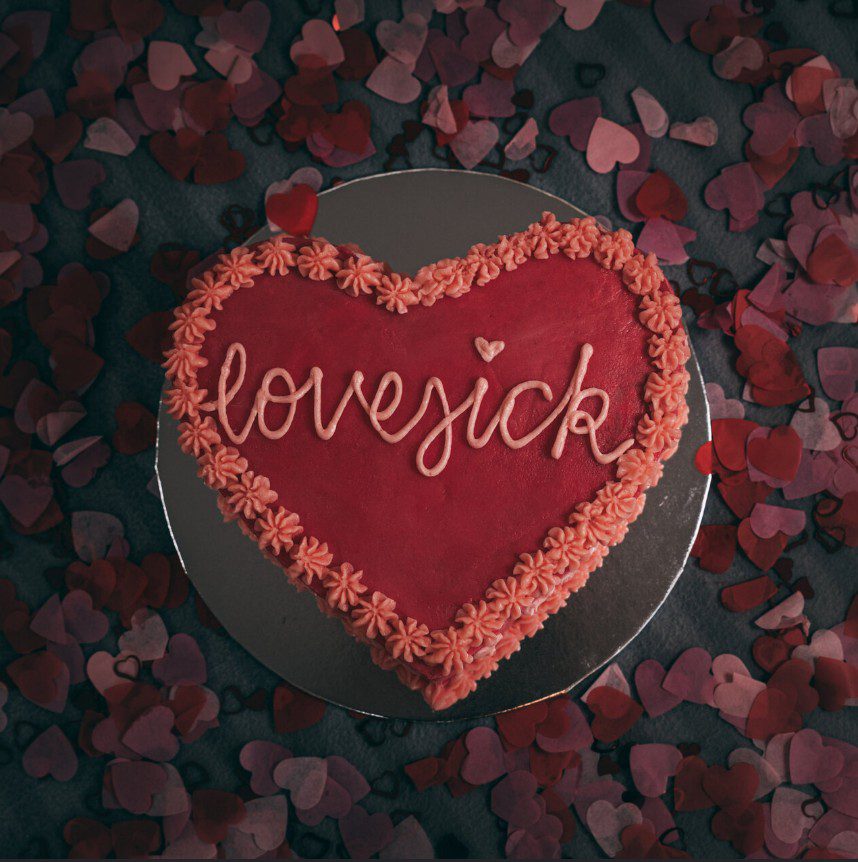 Heart shaped cake with the word lovesick written on it. 