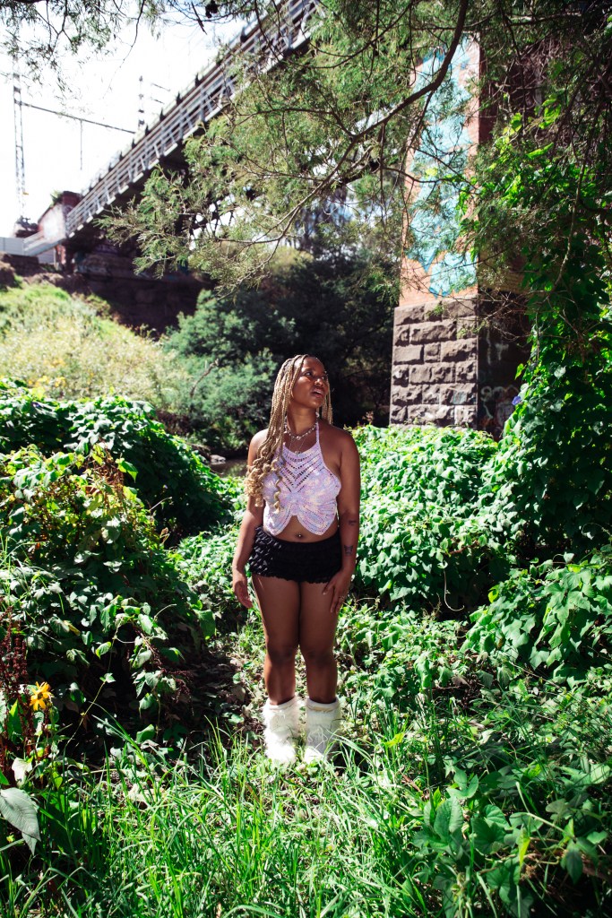 Jewel Owusu in front of a bridge with trees and bushes in the background