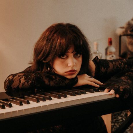 Image of Lara Buchanan leaning on a piano. Ep Cover for All That Glitters
