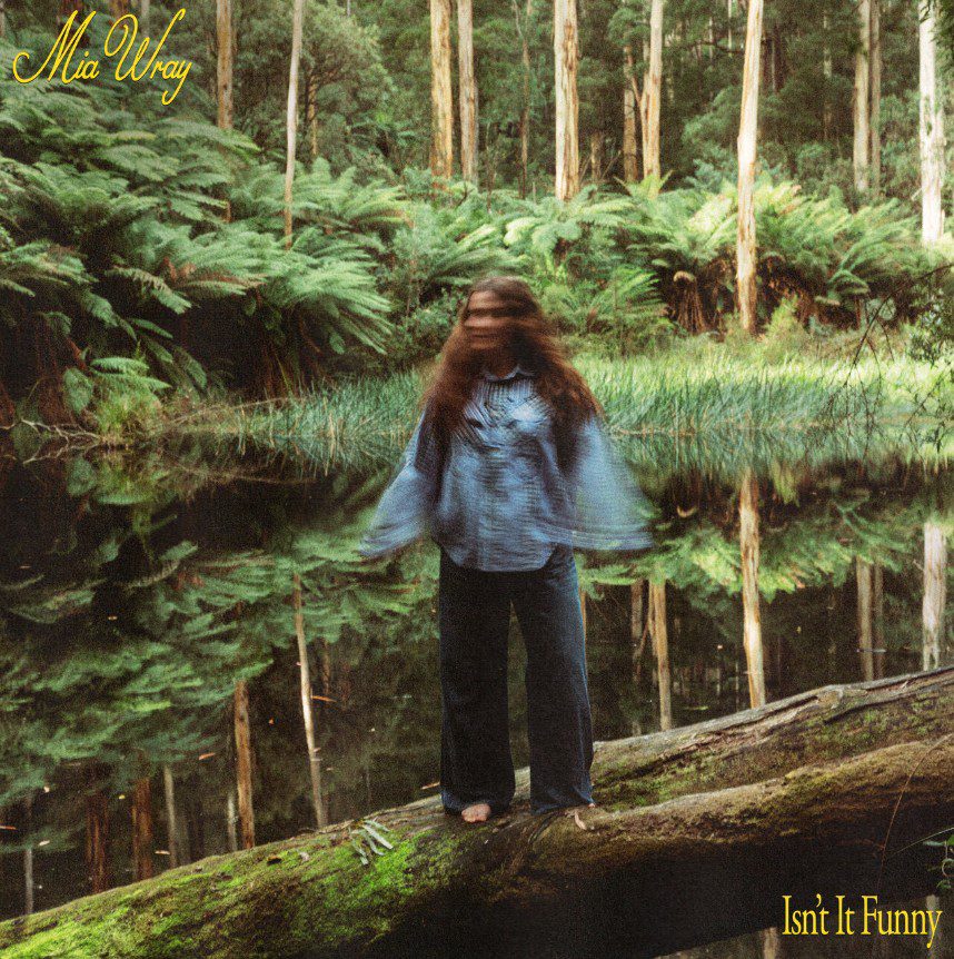 A blurry image of Mia Wray in front of a lake and a forest. Single cover for Mia Wray isn't it funny