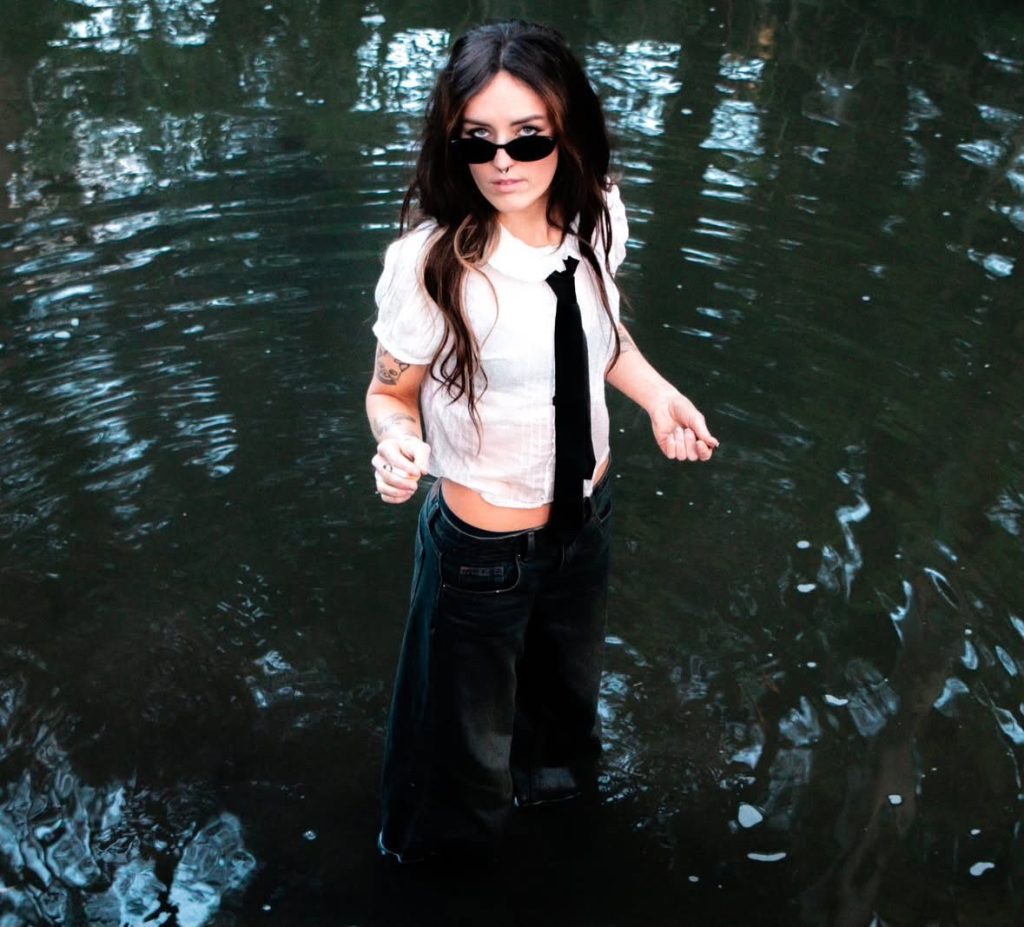 Birdgirl standing in a shallow body of water.