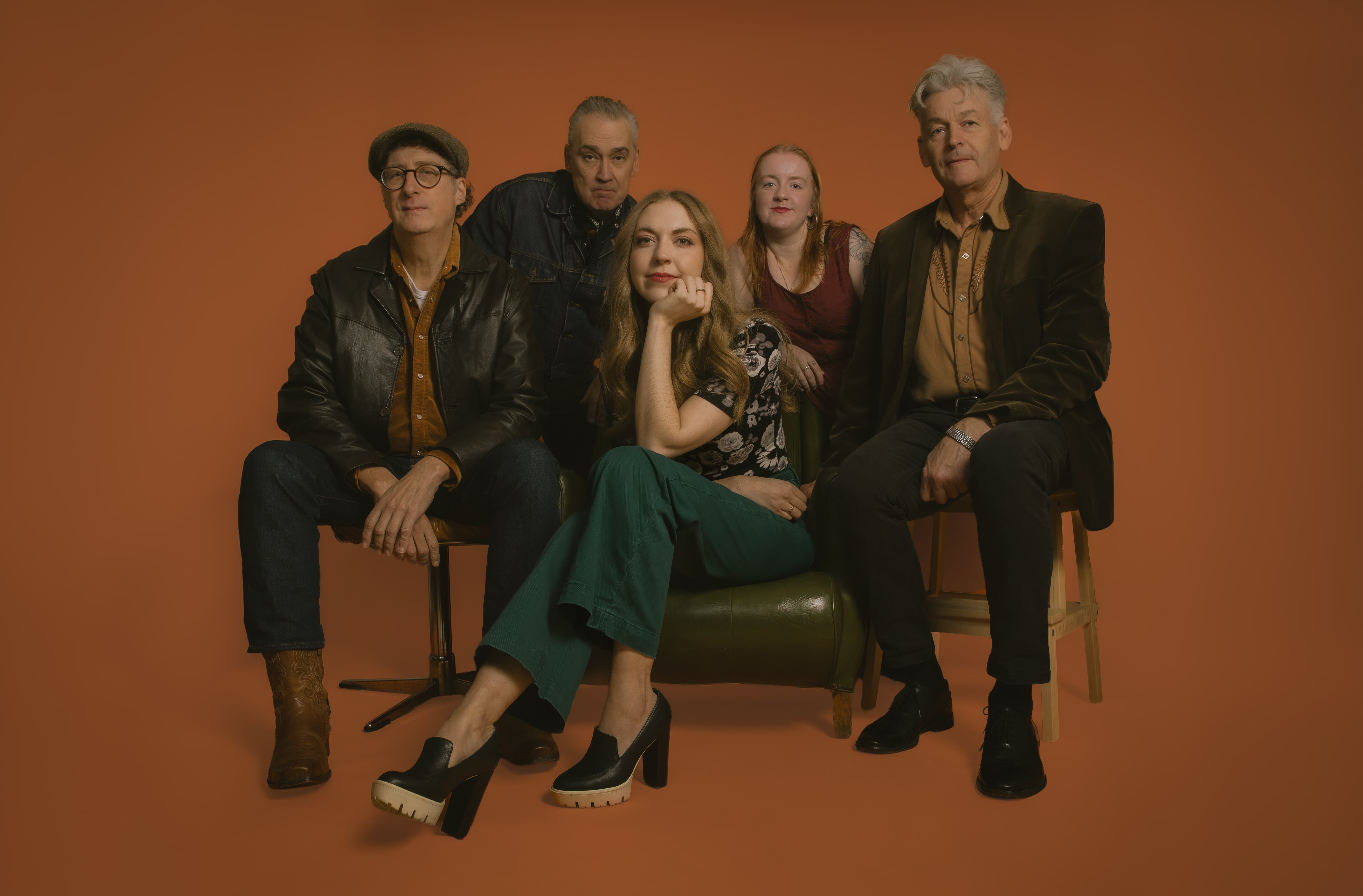 Image of Rhiz and The Sugarplums seated on various seats against an orange background