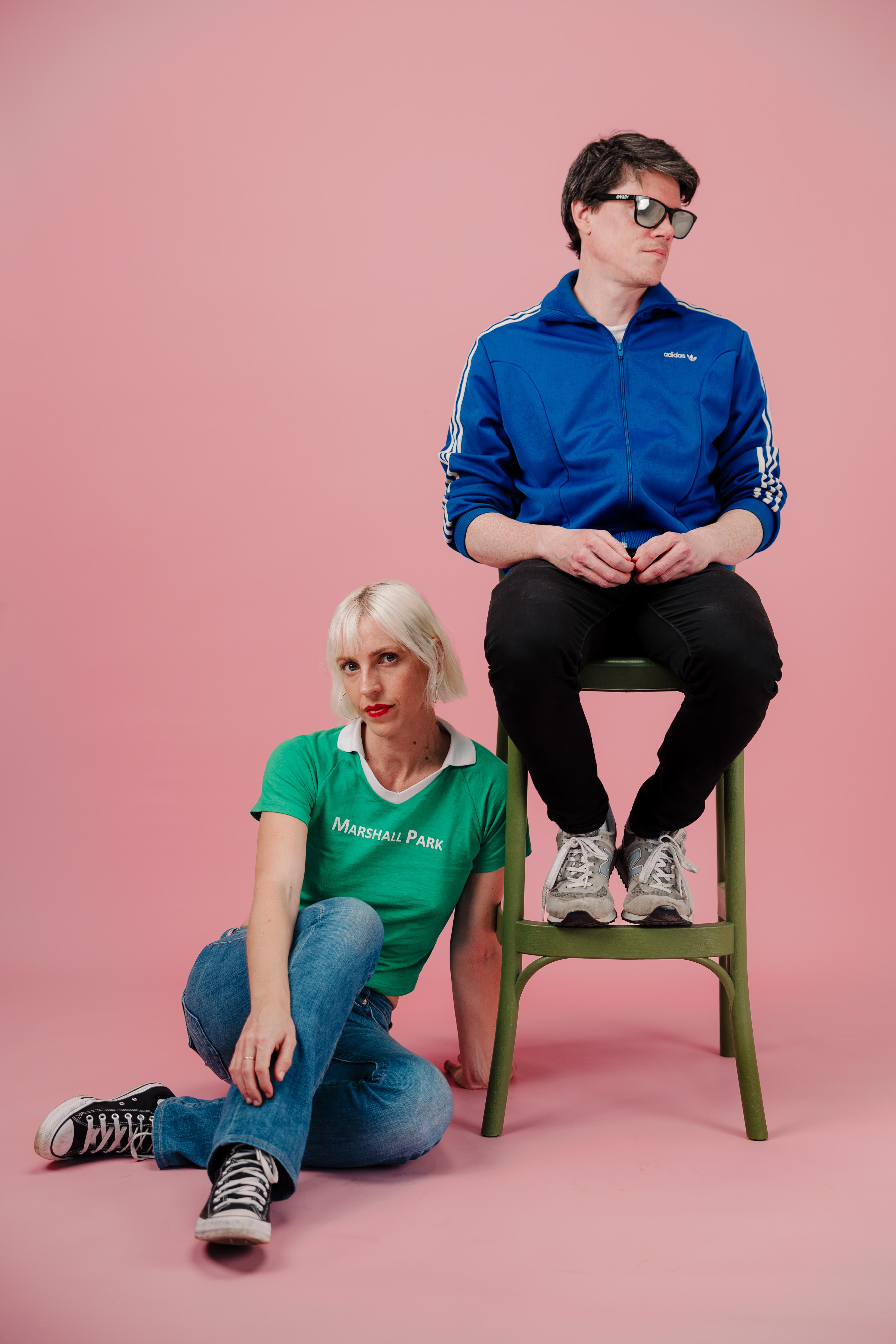 Image of the tryouts against a pink background. One person seated on a chair, the other on the floor.